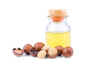 Bottle of macadamia oil with nuts and a cracked shell.